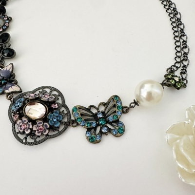 Colar metal escuro com borboleta azul verde, flores esmaltadas, pérola e pendente em forma de flor branco.