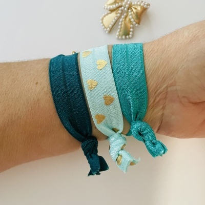 Pulseiras de tecido em azul e verde com detalhes dourados, e broche de laço com pérolas