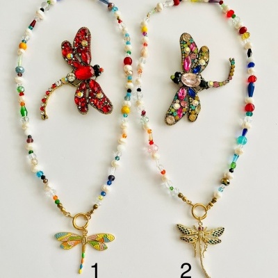 Dois colares com contas coloridas e pingentes de libélulas ao lado de dois broches de libélulas coloridos