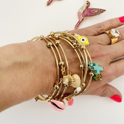 Pulseiras douradas com pendentes coloridos em mão feminina com anel e unhas vermelhas