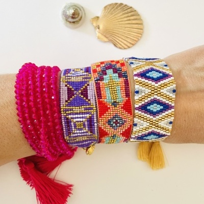 Braças de miçangas coloridas com padrões geométricos e pulseiras de fios rosa com franjas sobre pulso