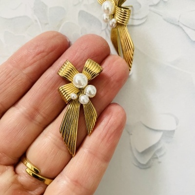 Brincos dourados em forma de laço com pérolas brancas