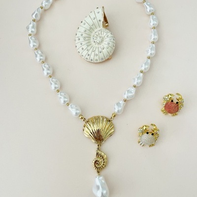 Conjunto de joias com colar de pérolas, brincos dourados e broche branco espiral