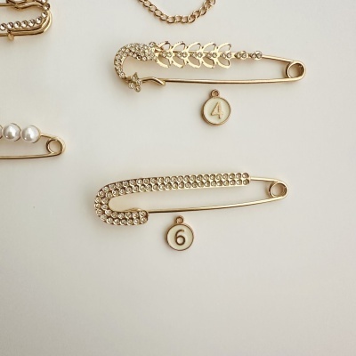 Dois alfinetes dourados com pedras brilhantes e pendentes numéricos 4 e 6.
