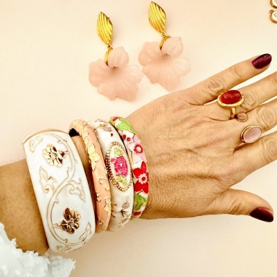 Pulseiras e anéis florais em tons de rosa, branco e dourado numa mão com unhas pintadas de vinho
