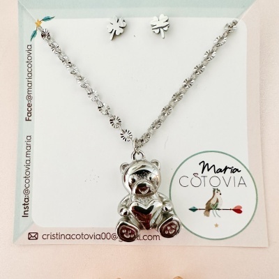 Conjunto de colar com pendente em forma de urso prateado e brincos flor prateados num cartão de marca