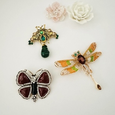 Broches de borboleta, abelha e libélula com pedras e flores decorativas brancas e rosa.