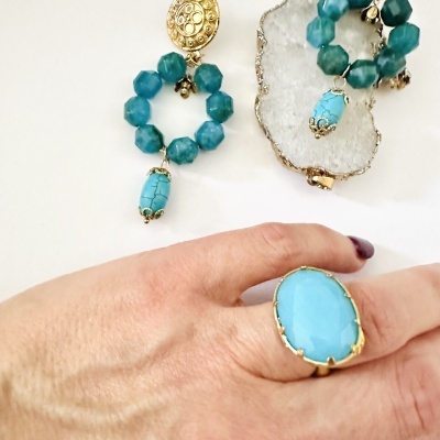 Brincos e anel de pedra azul e detalhes dourados com pedra branca no fundo