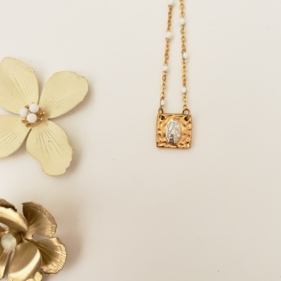 Colar dourado com pendente quadrado texturizado e folha prateada, decoração de flores no fundo