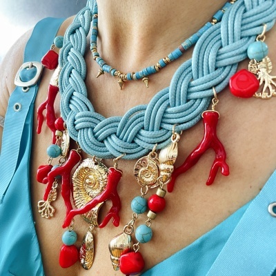 Colar azul claro trançado com pendentes vermelhos e dourados em tecido junto ao pescoço