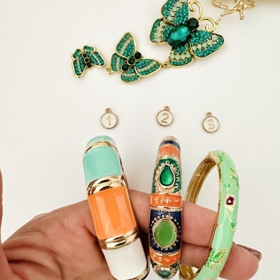 Pulseiras esmaltadas coloridas e colar com borboletas verdes sobre fundo branco.