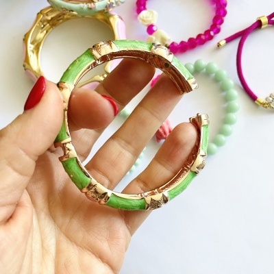 Pulseira verde com detalhes dourados em forma de bambu segurada por mão