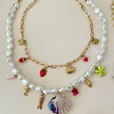 Colares com pérolas brancas e pendentes coloridos, e colar dourado com figuras pequenas e morangos.