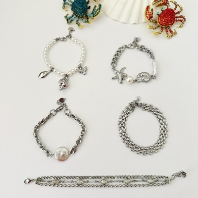 Pulseiras de metal prateado com pérolas e broches de caranguejo em metal dourado com cristais coloridos