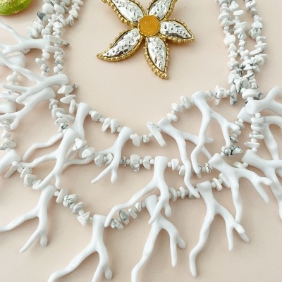 Colar branco com pendente flor dourada e prateada sobre fundo bege