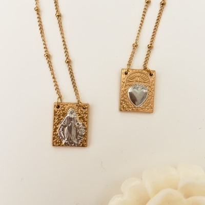 Dois colares dourados com pendentes retangulares decorativos, fundo branco e flor branca