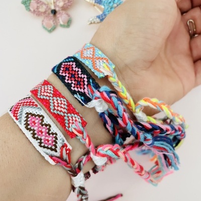 Pulseira trançada colorida artesanal no pulso com fundo branco e decoração de borboleta e estrela do mar.