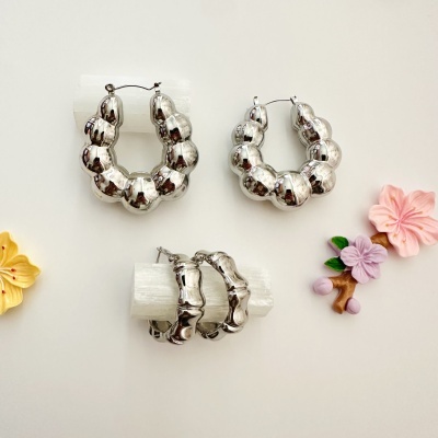 Brincos de argola prateada com design arredondado sobre suportes brancos e flores decorativas coloridas.