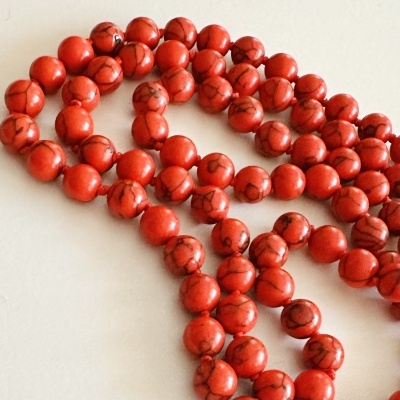 Colar de contas vermelhas com veios escuros sobre superfície clara