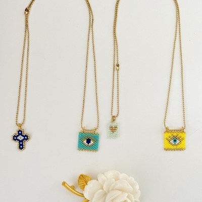 Quatro colares dourados com pingentes coloridos de miçangas sobre fundo branco e flor branca decorativa