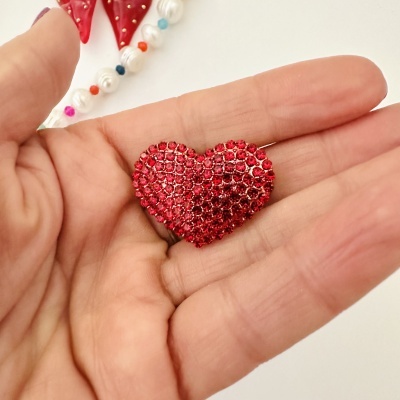 Coração em strass vermelhos em mão com pérolas e contas coloridas no fundo