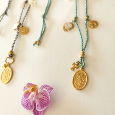 Colares com medalhões dourados e flor de orquídea lilás sobre fundo branco