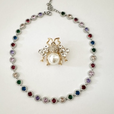 Colar colorido e broche de abelha com pérola em fundo branco