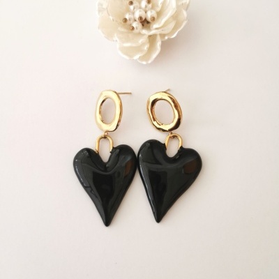 Brincos pendentes em forma de coração preto e base dourada com ornamento floral ao fundo
