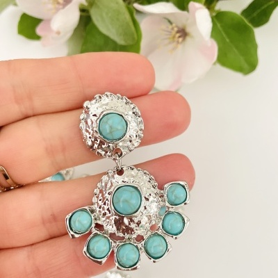 Brincos prateados com pedras azul-turquesa e flores ao fundo
