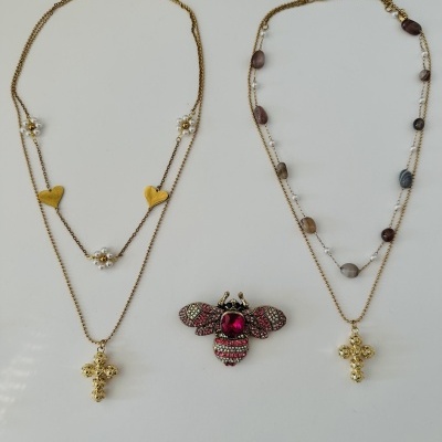 Dois colares dourados com cruz e um broche em forma de abelha com pedras cor-de-rosa e vermelhas