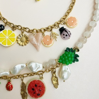 Colares e brincos com pendentes em forma de frutas coloridas e outros elementos, sobre fundo branco.