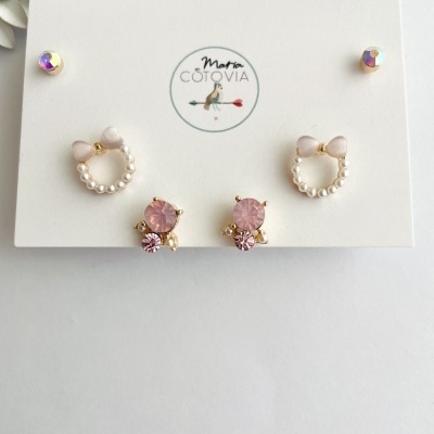 Conjunto de três pares de brincos em cartão branco com logotipo e pedras rosa