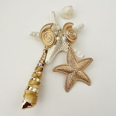 Brincos dourados com formas de caracol e estrela-do-mar sobre estrela-do-mar branca e concha pequena