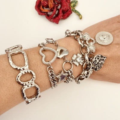 Pulseiras prateadas com vários pendentes no pulso e rosa vermelha decorativa