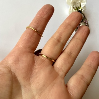 Mão feminina com duas argolas douradas e acessório floral ao fundo