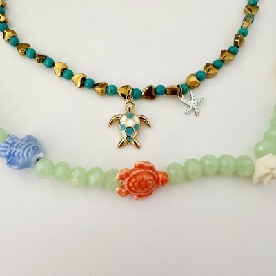 Duas pulseiras com contas coloridas, tartaruga dourada, estrela-do-mar e peixe azul em fundo branco