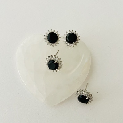 Brincos com pedras pretas e cristais sobre base branca em forma de coração.