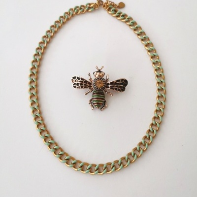 Colar dourado e verde com pendente de abelha detalhado sobre fundo branco