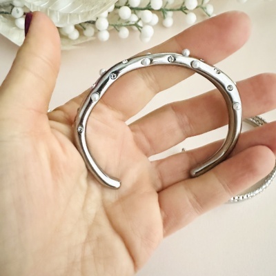 Pulseira prateada com pérolas e pedras brilhantes numa mão