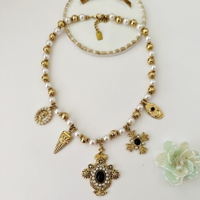 Conjunto de colar e pulseira com contas e pendentes dourados e brancos sobre fundo branco com flor verde-claro