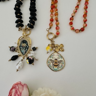 Duas pulseiras com contas e pingentes coloridos em fundo branco com flores.