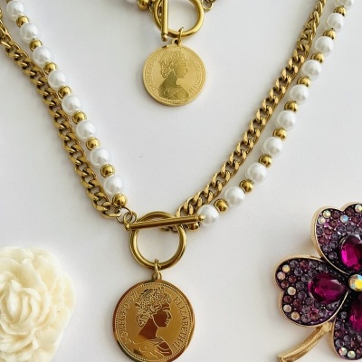 Colares com corrente dourada, pérolas brancas e medalhões com perfil da rainha Elisabeth II junto a broche de trevo com pedras coloridas