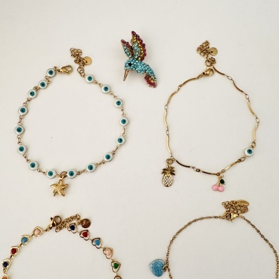 Pulseiras douradas com pendentes coloridos e brincos de beija-flor com strass coloridos