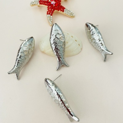 Brincos em forma de peixe prateado e broche estrela-do-mar vermelho com pedras brilhantes sobre concha branca