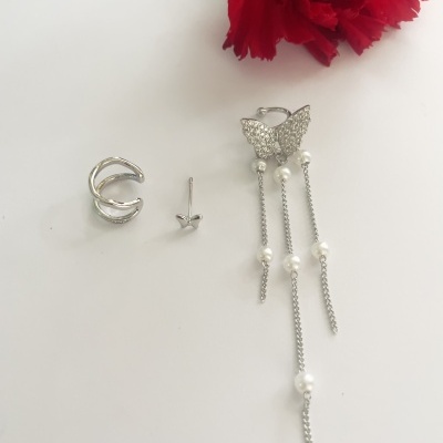 Três brincos prateados com detalhes em pérolas, borboleta e flor vermelha ao fundo