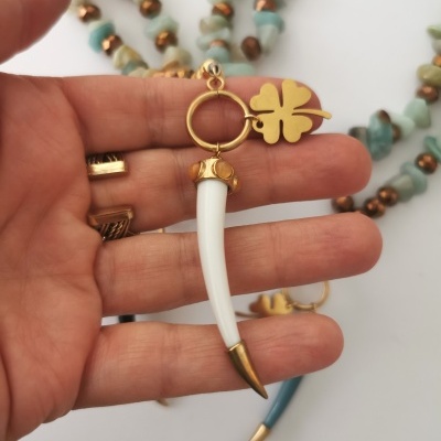 Brincos com dentes longos bege e dourados e pingente de folha de trevo dourada