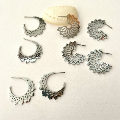 Oito pares de brincos de metal prateado com padrões recortados sobre superfície clara
