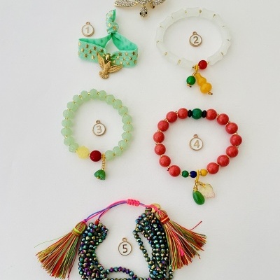Cinco peças de bijuteria dispostas sobre fundo branco, incluindo pulseiras coloridas e broche dourado