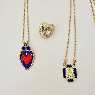 Três peças de joalharia: colar com pendente coração em azul e vermelho, anel dourado com pedra transparente, colar dourado com pendente retangular azul