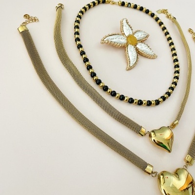 Conjunto de colar e pulseiras douradas com pendentes em formato de coração e flor em fundo claro